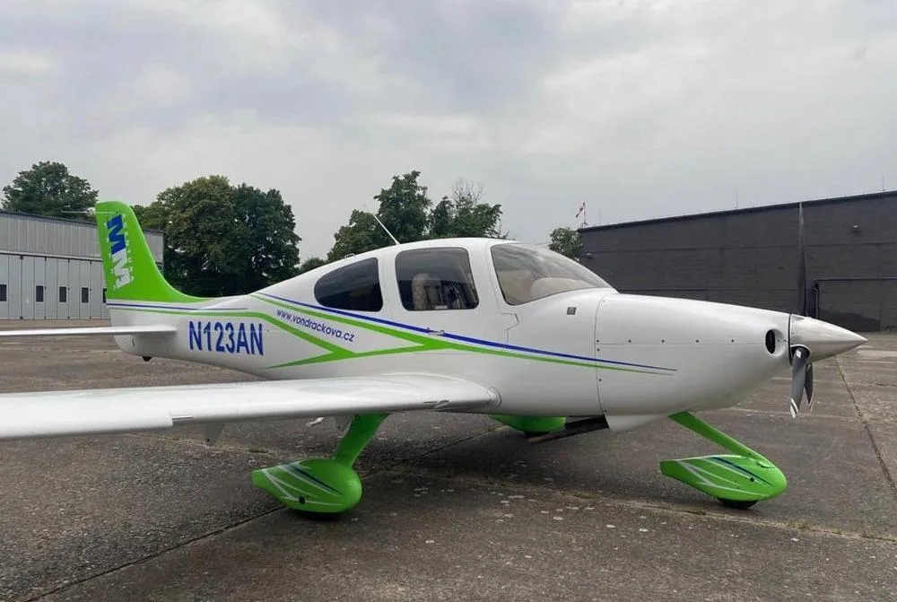 A white and green single-engine propeller aircraft, N123AN, parked on an asphalt apron under a cloudy sky.