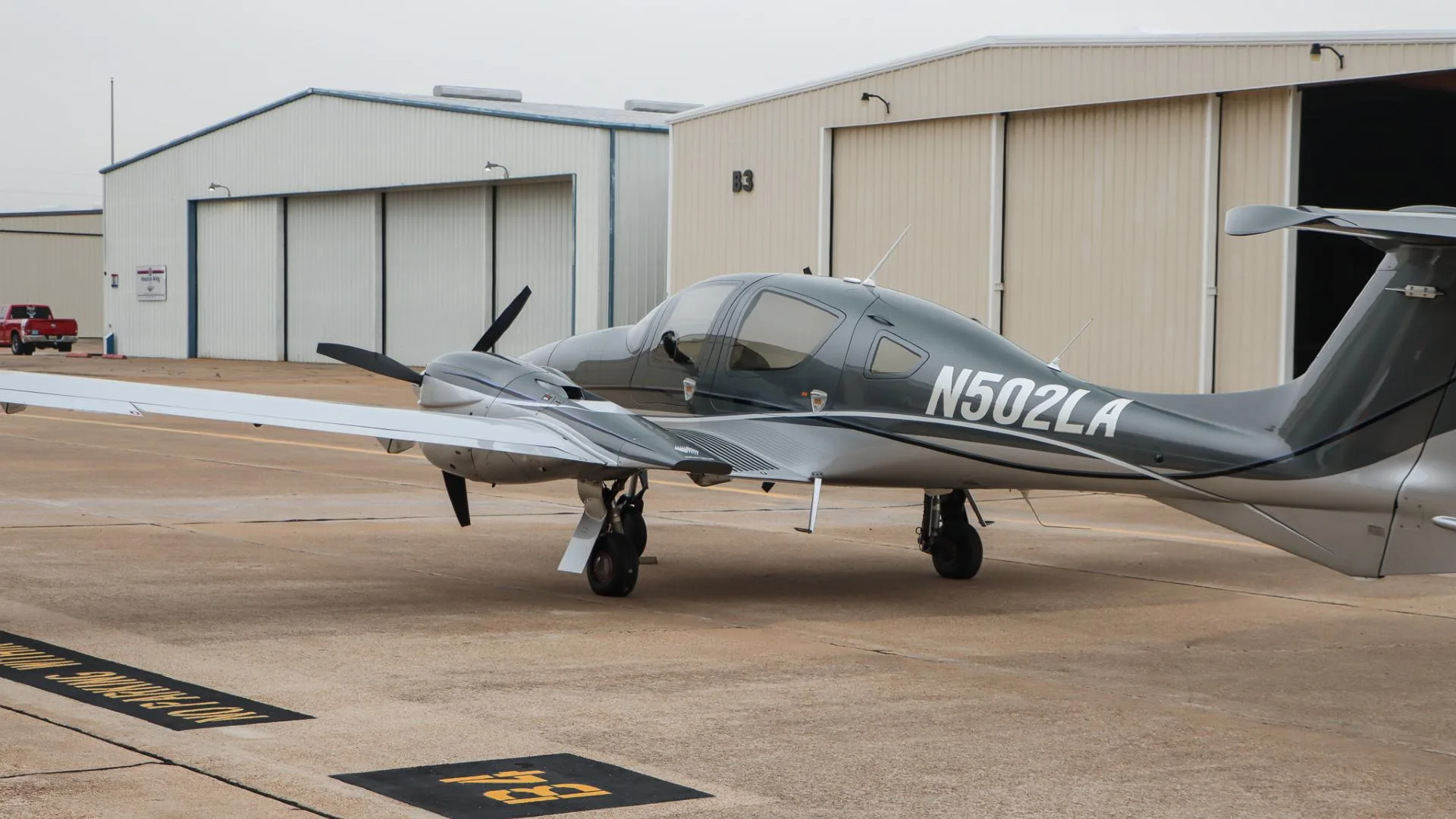 A side view of the gray and silver Diamond DA62 aircraft, N502LA, parked on an airport tarmac.