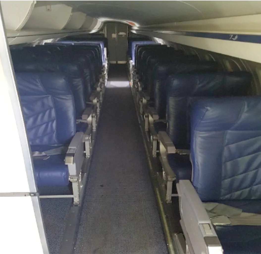A view down the aisle of an aircraft cabin, showing multiple rows of blue passenger seats.