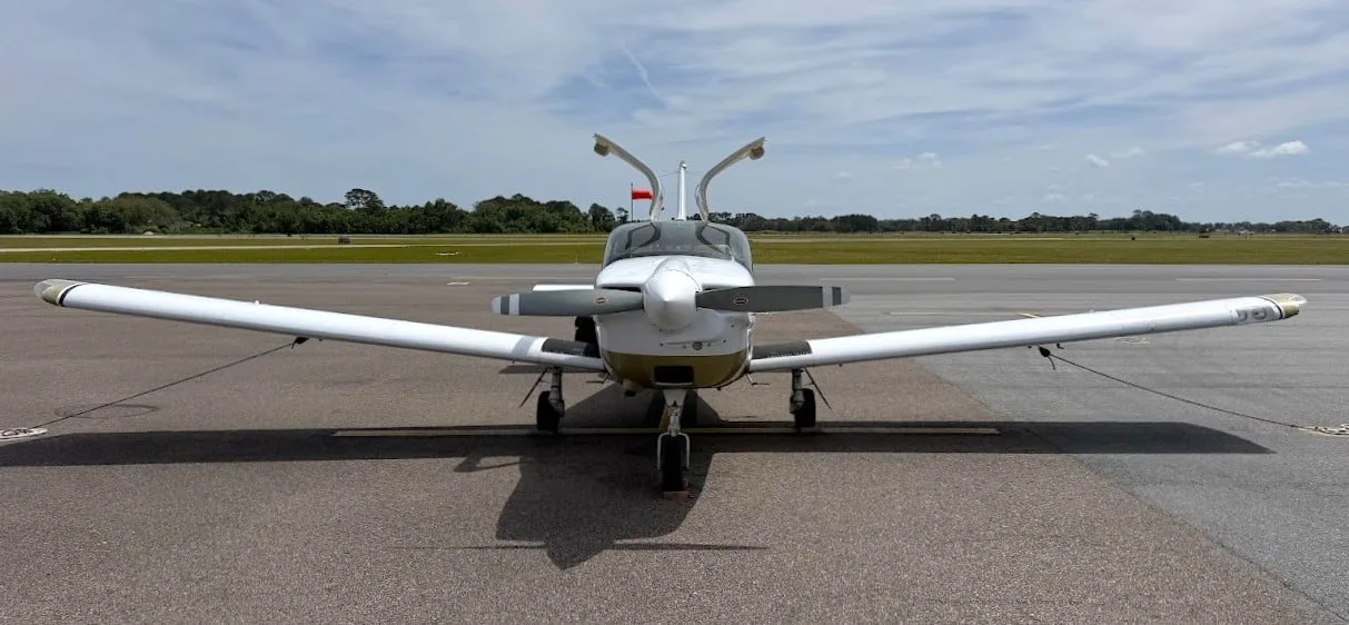 A head-on view of the white and gold Socata TB-20 Trinidad aircraft with its doors open on an airfield.