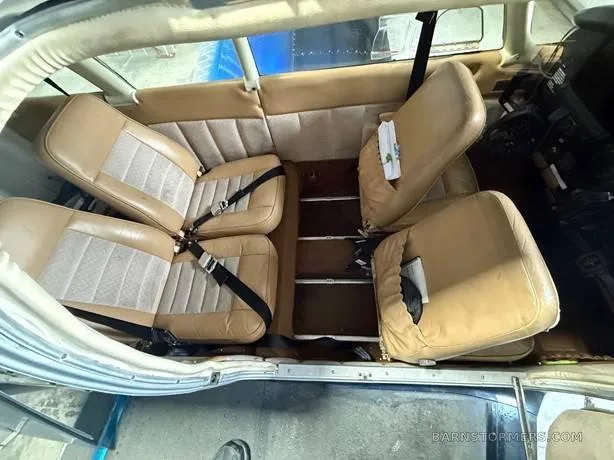 The tan and beige interior cabin of a small aircraft, showing four seats with seatbelts.
