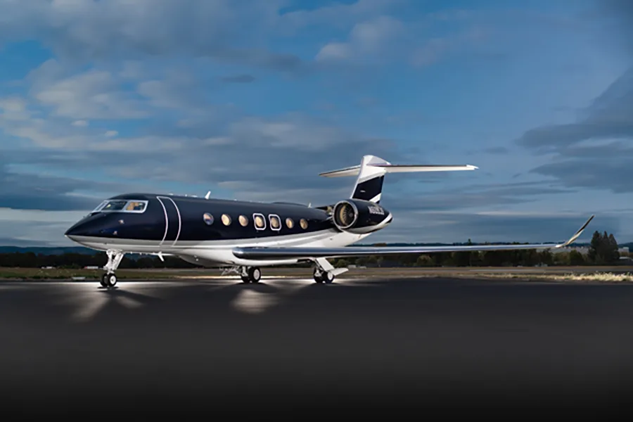 A dark blue and white Gulfstream G650 business jet, tail number N609JS, parked on a tarmac at dusk with landing lights on.