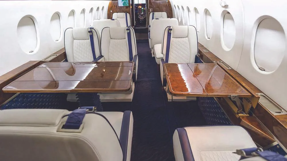 The aircraft cabin interior shows white seats with blue accents and two fold-out wooden tables.