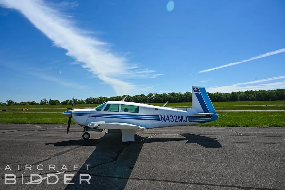 A white single-engine propeller aircraft with blue stripes and registration N432MJ is parked on an asphalt runway.
