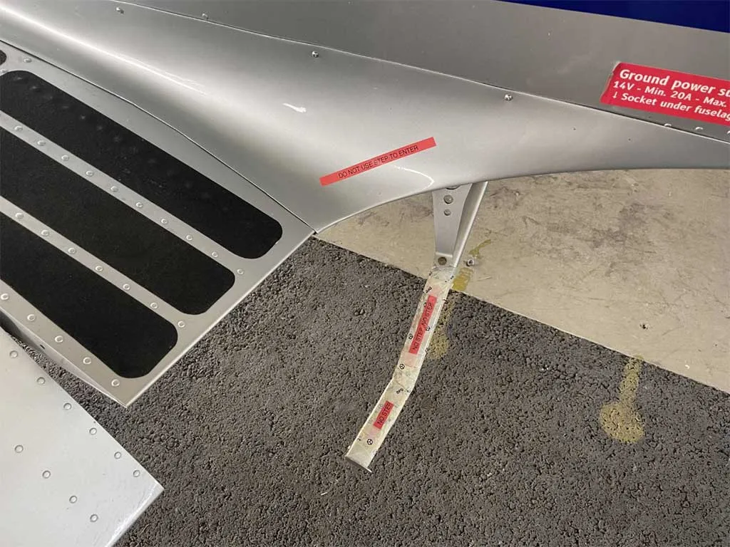 Close-up of the silver fuselage showing a step, ground power socket, and warning labels.