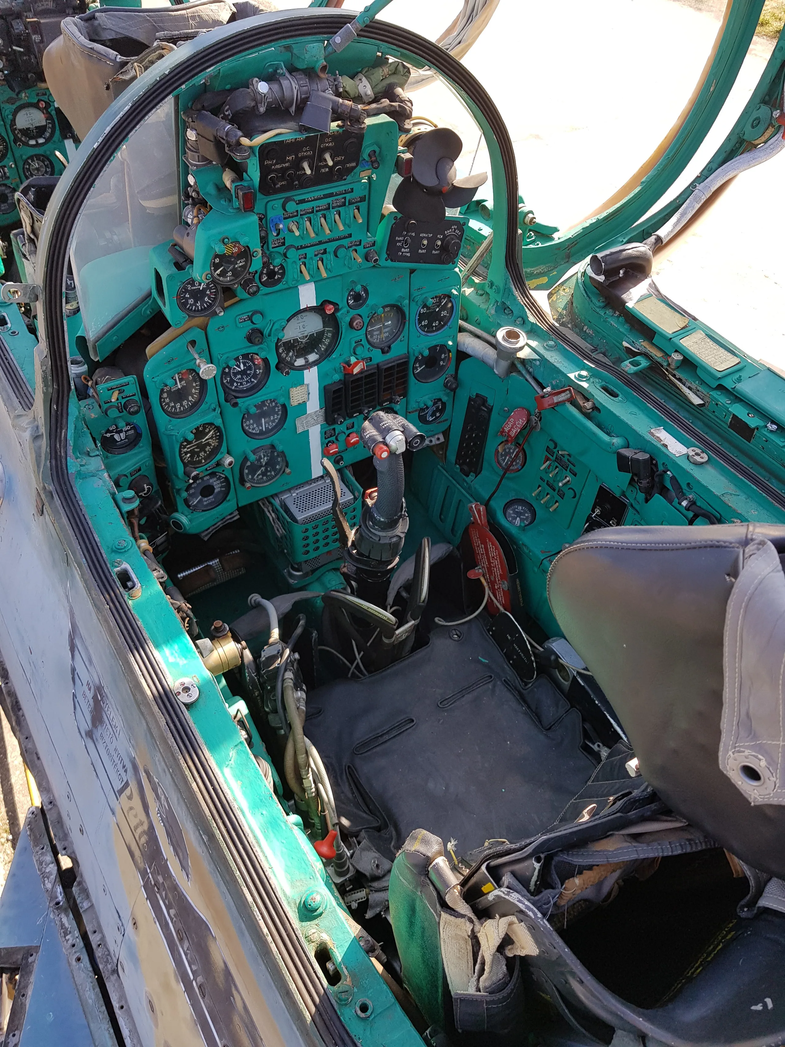 The detailed cockpit of a MiG-21 fighter jet, showing the green instrument panel, control stick, and pilot's seat.