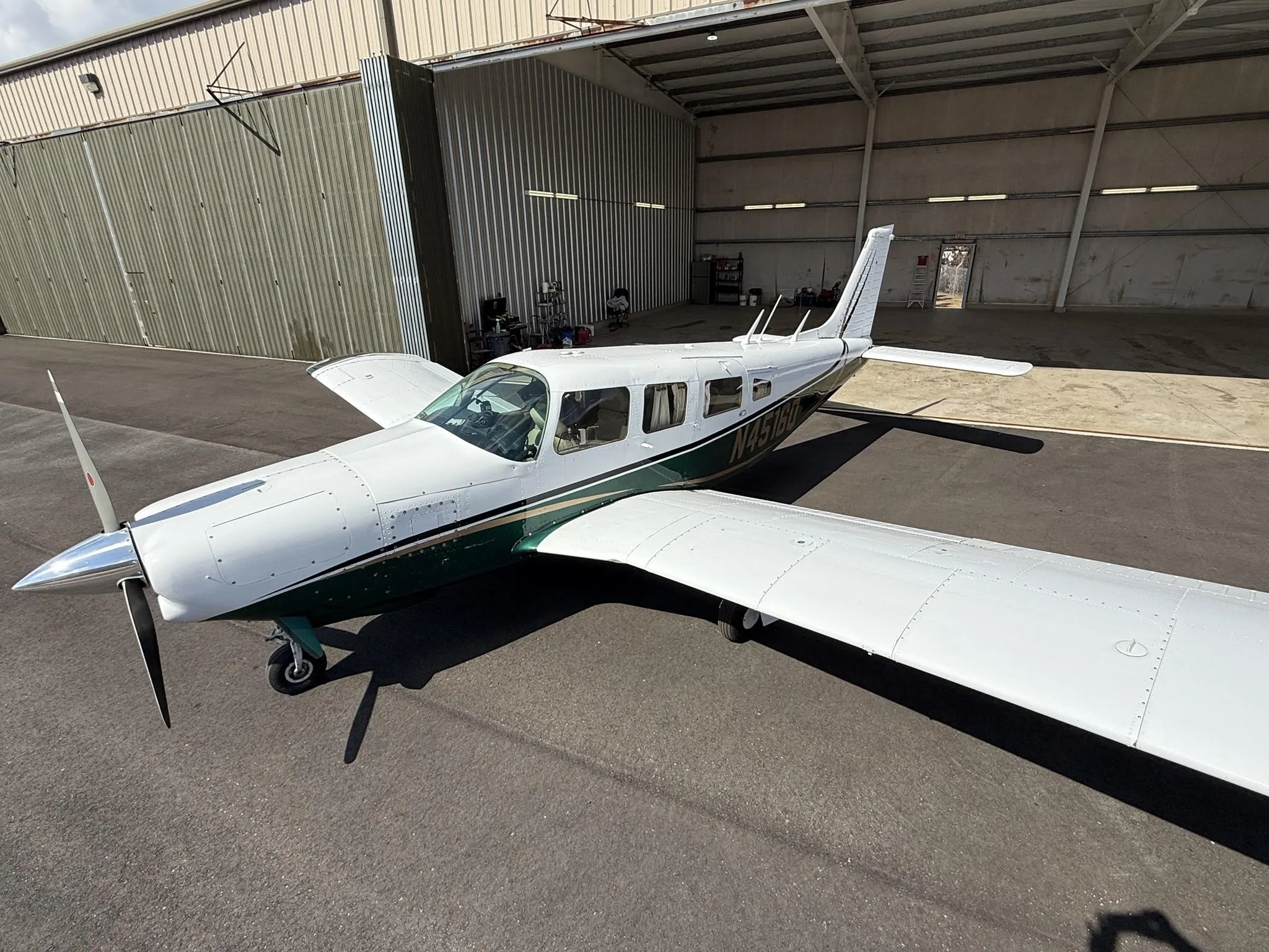 A white and green single-engine propeller aircraft, N4518Q, is parked on an asphalt apron in front of an open hangar.