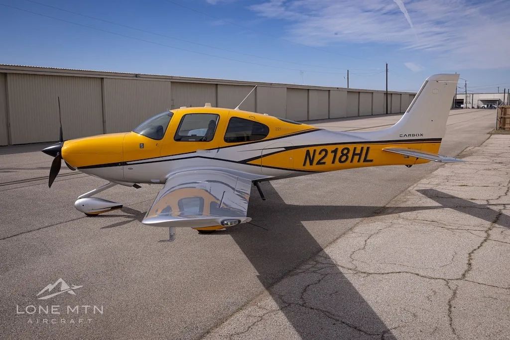 A Cirrus SR22 aircraft with yellow and silver paint scheme parked on an airfield, showing the right side.
