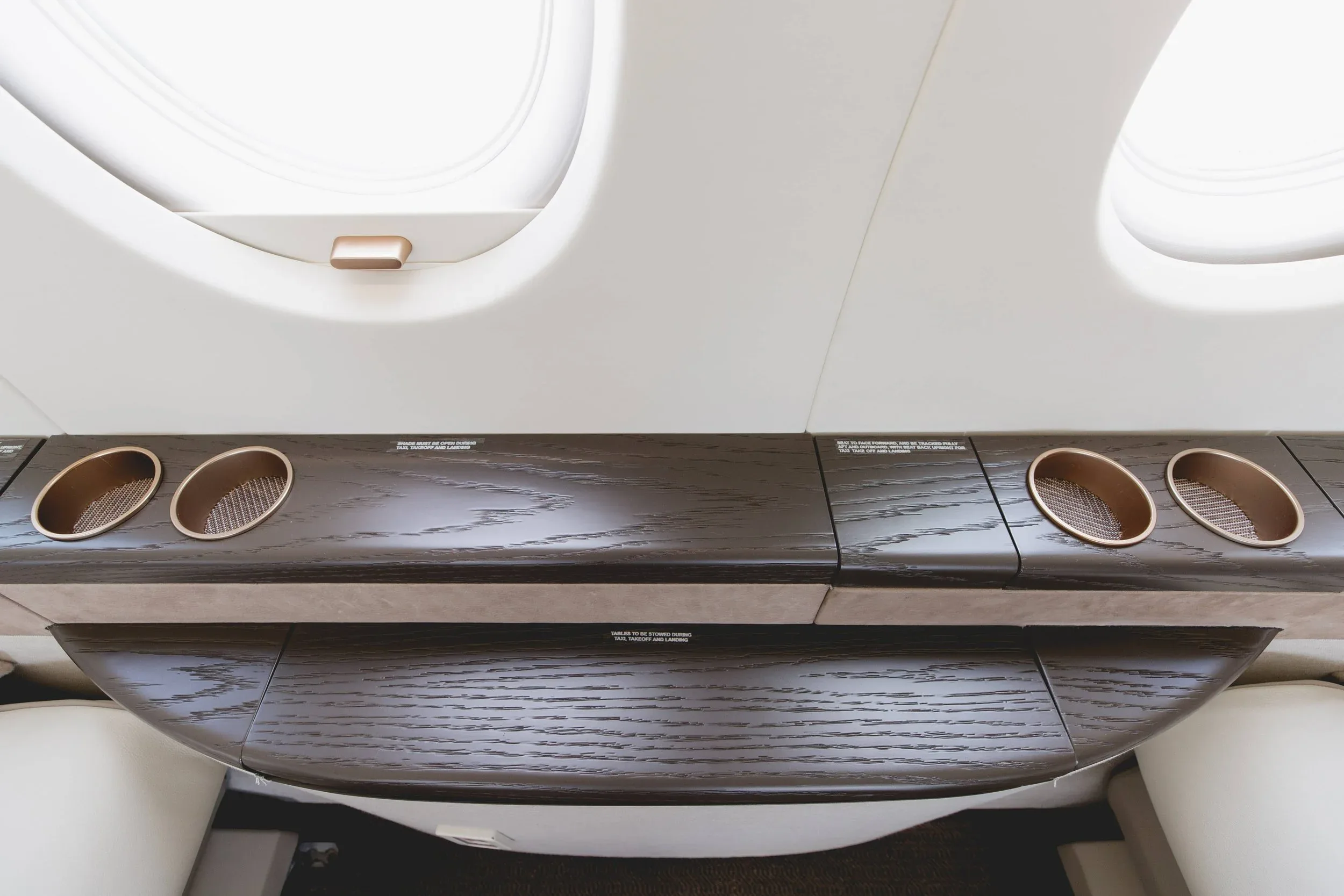 An overhead view of the private jet cabin's dark wood paneling with integrated cup holders and window shades.