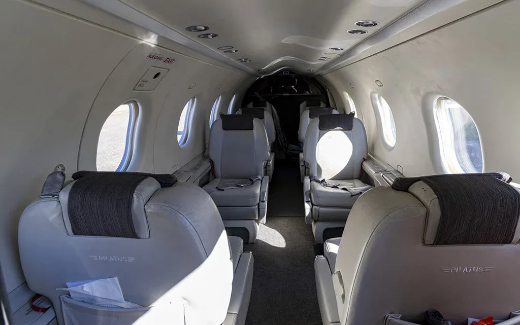 The light grey passenger cabin of a Pilatus PC-12 aircraft, showing multiple rows of seats and windows.