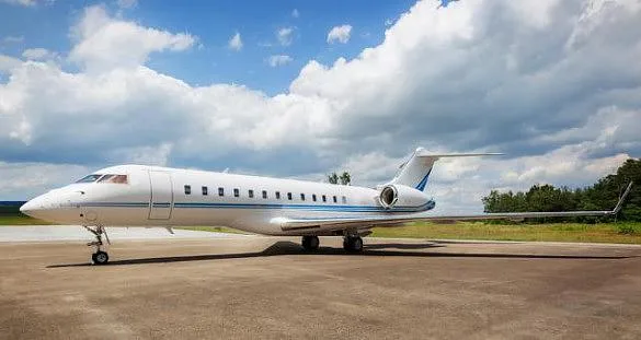 A white business jet with blue accent stripes is parked on a tarmac under a partly cloudy sky.