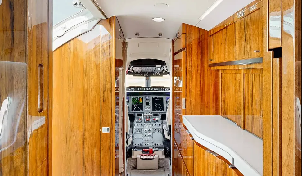The elegant galley area of a private jet with glossy wood paneling, looking towards the cockpit.