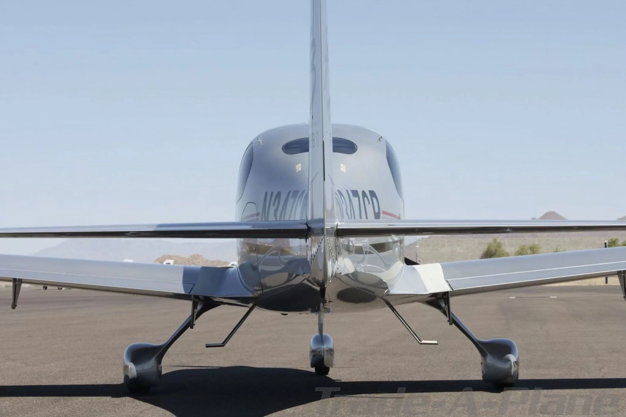 A rear view of the silver Cirrus SR22 aircraft showing its tail and horizontal stabilizers.