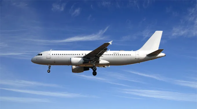 A white Airbus A320 aircraft with landing gear extended, flying against a blue sky with light clouds.