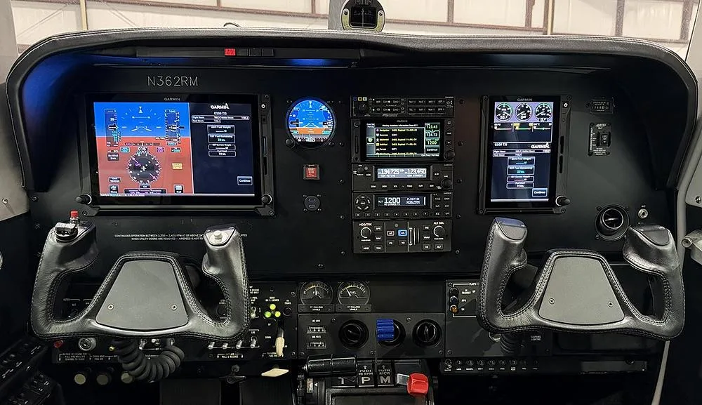 The cockpit instrument panel of an aircraft, featuring multiple Garmin glass displays and two control yokes.