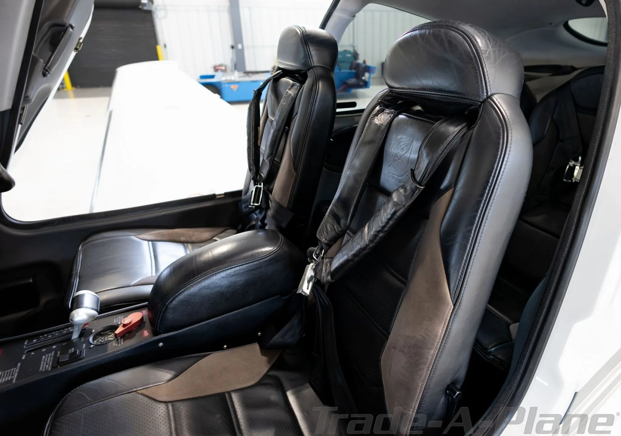 The front two black leather seats with grey accents and seatbelts in the Cirrus SR22 aircraft cabin.