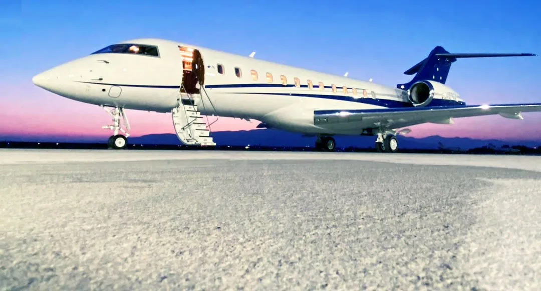 A white and blue business jet, N59GX, with its door open and stairs extended, sits on a tarmac at sunset.