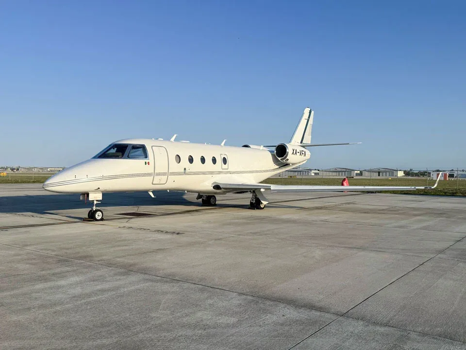 A white business jet with green stripes on the tail, registration XA-VFN, parked on a tarmac under a clear blue sky.