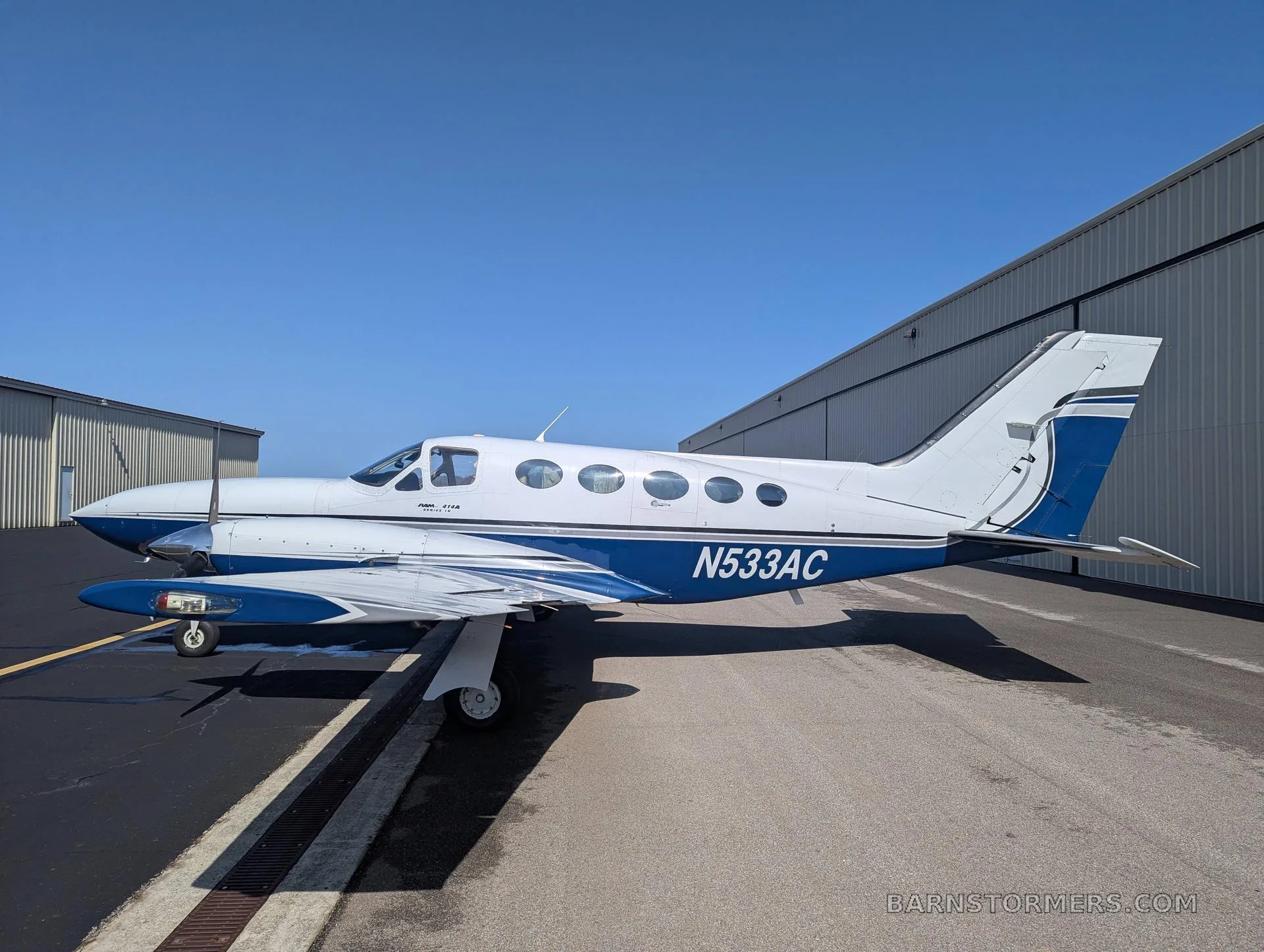 A white and blue twin-engine propeller aircraft (Cessna 414 Chancellor) with tail number N533AC parked on an asphalt ramp, viewed from the front-right side.