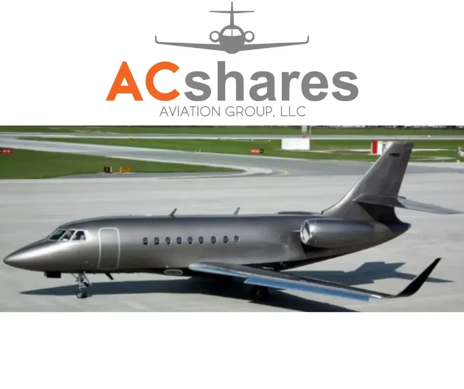 A dark metallic grey business jet, likely a Dassault Falcon, parked on an airport tarmac.