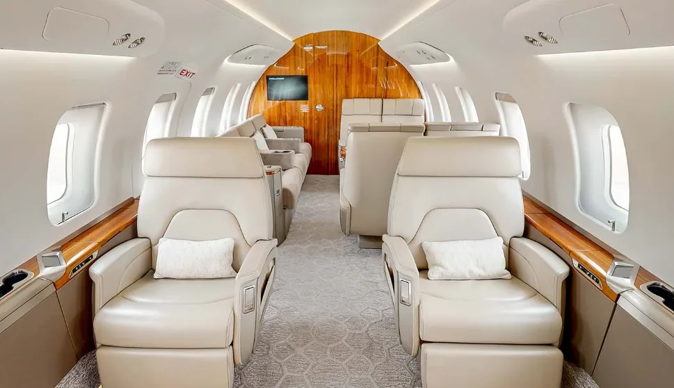 The luxurious main cabin of a private jet featuring beige leather seats and polished wood accents.