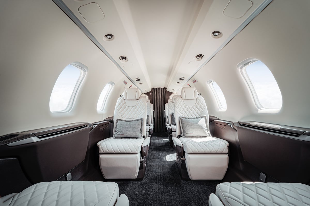 The interior of the aircraft features white leather seats and dark wood trim.