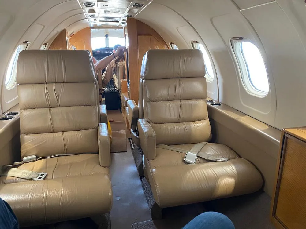Interior view of an aircraft cabin with two rows of tan leather seats facing forward.