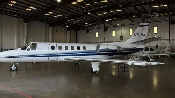 A white business jet with blue stripes, tail number N51DA, parked inside a hangar.