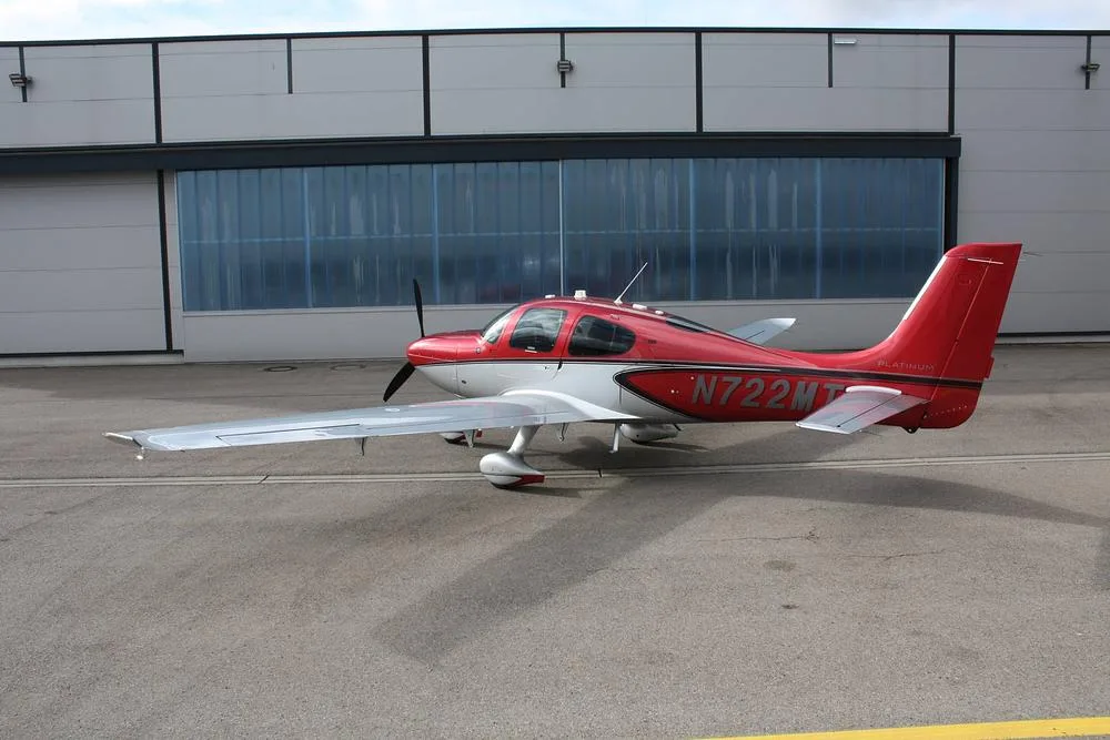 A red and white Cirrus SR22 aircraft, registration N722MT, parked on an asphalt apron with its wings extended.