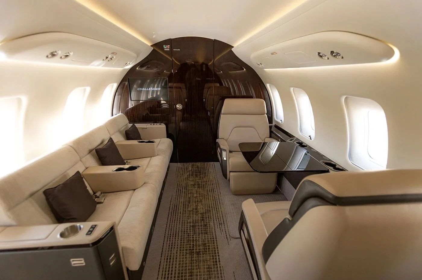 The spacious cabin interior of a business jet, featuring a long beige sofa, a table, and individual seats.