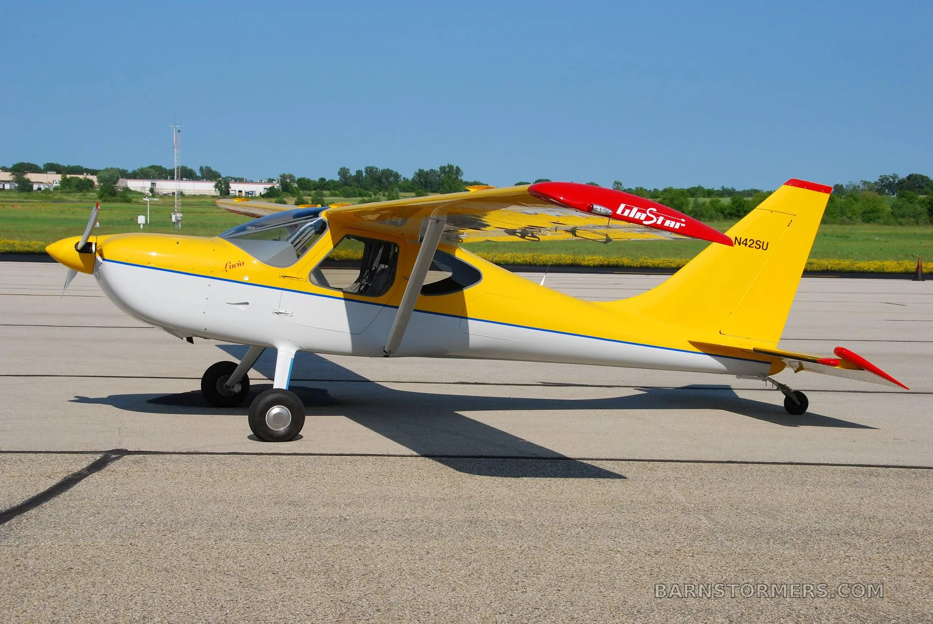 A yellow and white light sport aircraft with red wingtips and tail, registration N42SU, parked on an asphalt runway under a clear blue sky.