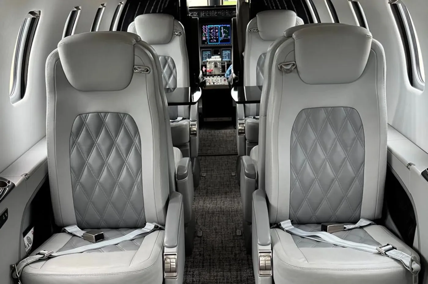The main cabin interior of a business jet, featuring light grey quilted leather seats with seatbelts.