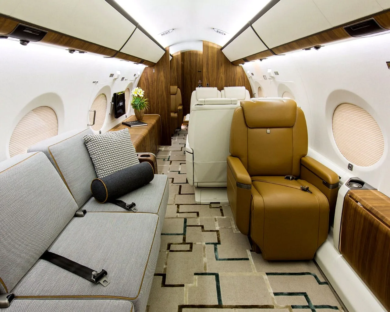 A private jet cabin interior featuring a grey sofa, a brown leather seat, and dark wood paneling.