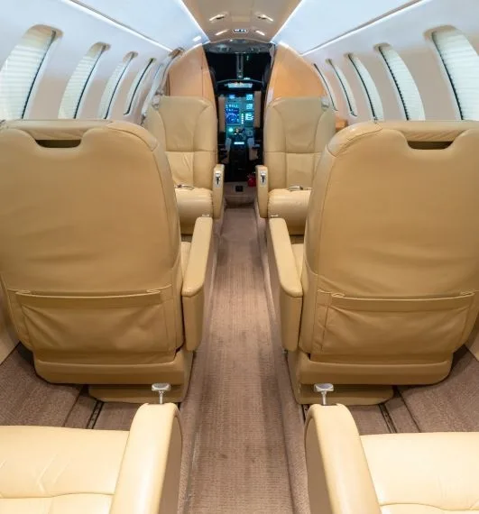 The interior cabin of a business jet features tan leather seats and a view towards the cockpit.