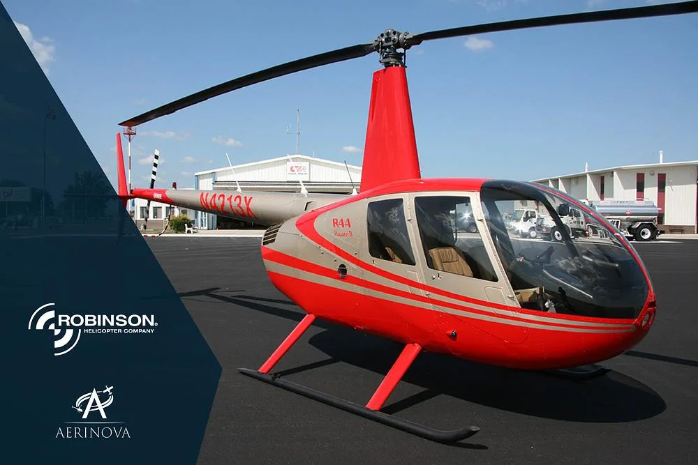 A red and silver Robinson R44 Raven II helicopter (N4213Y) is parked on an asphalt apron with hangars in the background.
