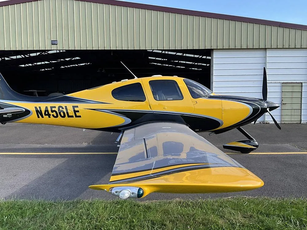 Side view of a yellow and black Cirrus SR22 aircraft with registration N456LE parked outside a hangar.