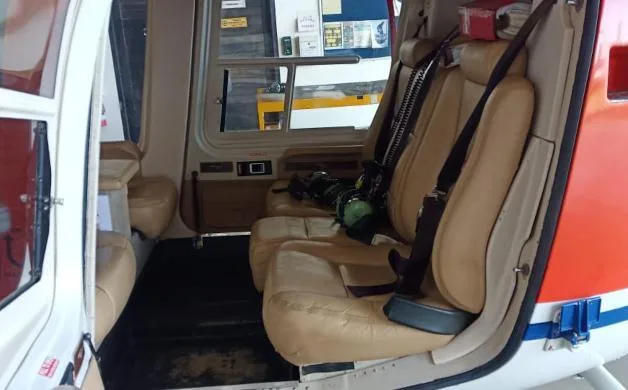 The helicopter cabin interior showing two tan leather passenger seats with seatbelts and an open door.