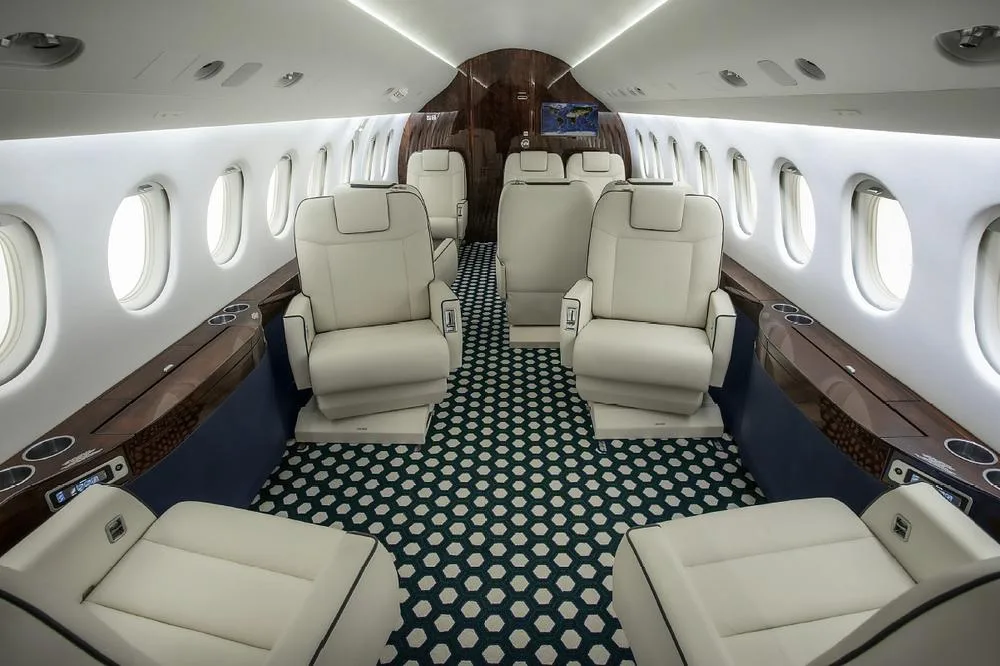 The luxurious interior cabin of a business jet with white leather seats and a patterned carpet.