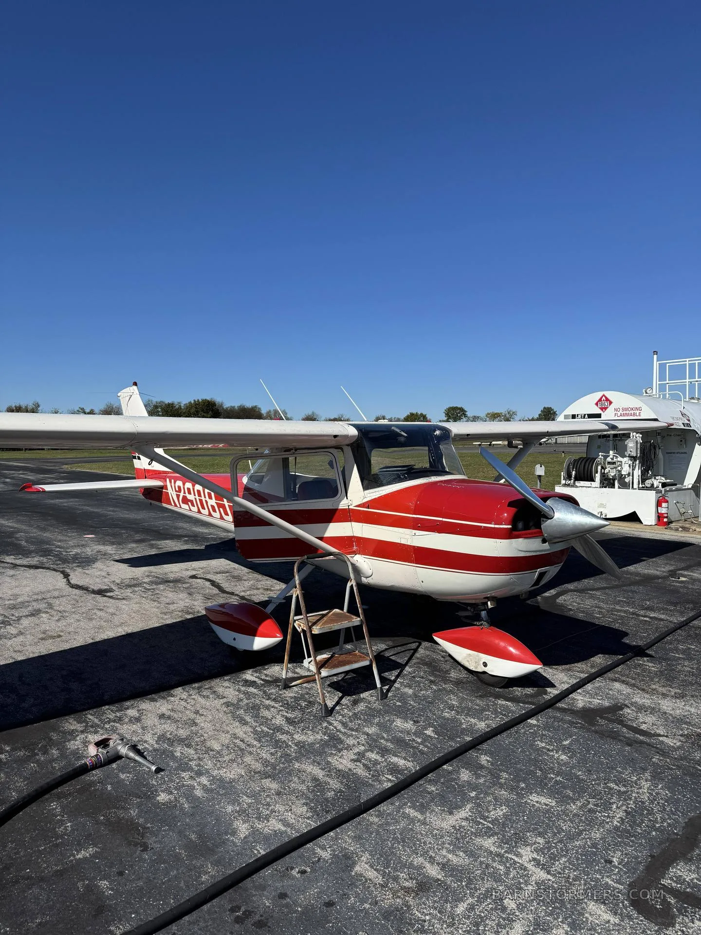 A red and white single-engine aircraft with registration N2908J parked on an airfield next to a fuel truck.