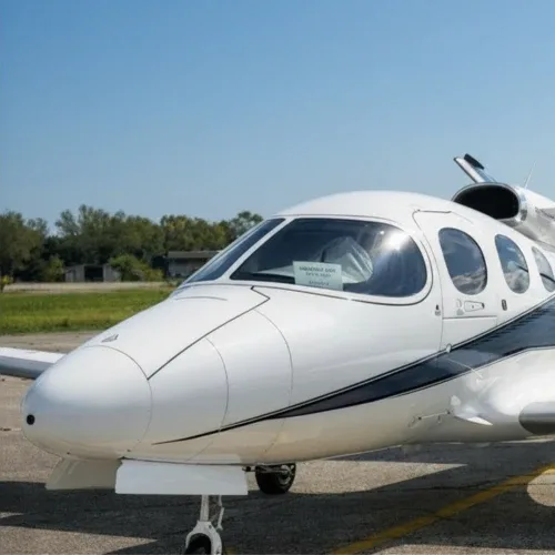 A white private jet with a dark stripe on the fuselage, parked on an tarmac under a clear blue sky.