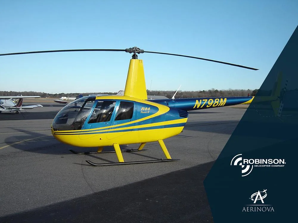 A yellow and blue Robinson R44 Raven II helicopter, registration N798M, parked on an asphalt tarmac under a clear sky.