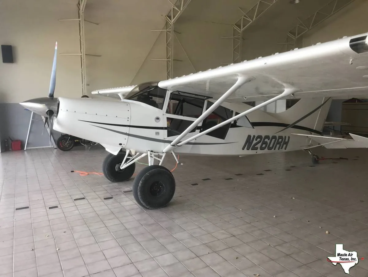 A white single-engine propeller aircraft with large tundra tires and black and grey stripes, registration N260RH, parked in a hangar.