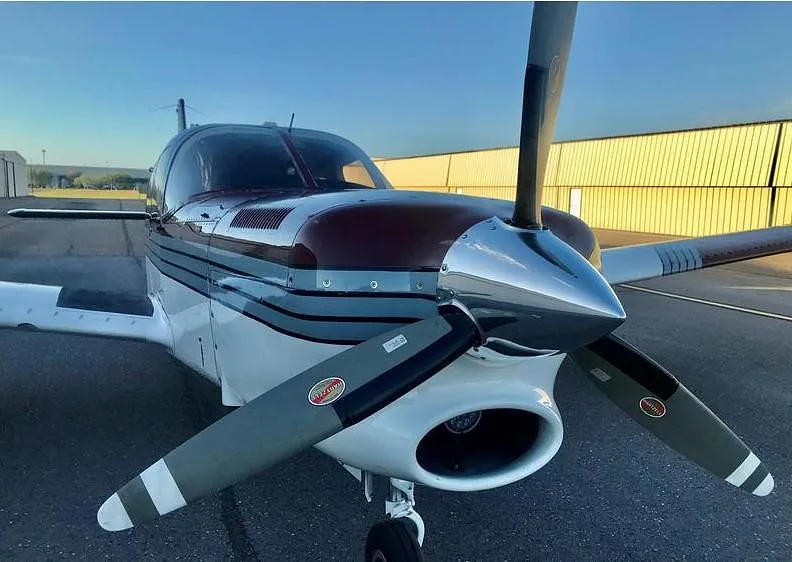A front view of the burgundy and white single-engine aircraft, N11HK, highlighting its propeller and nose.