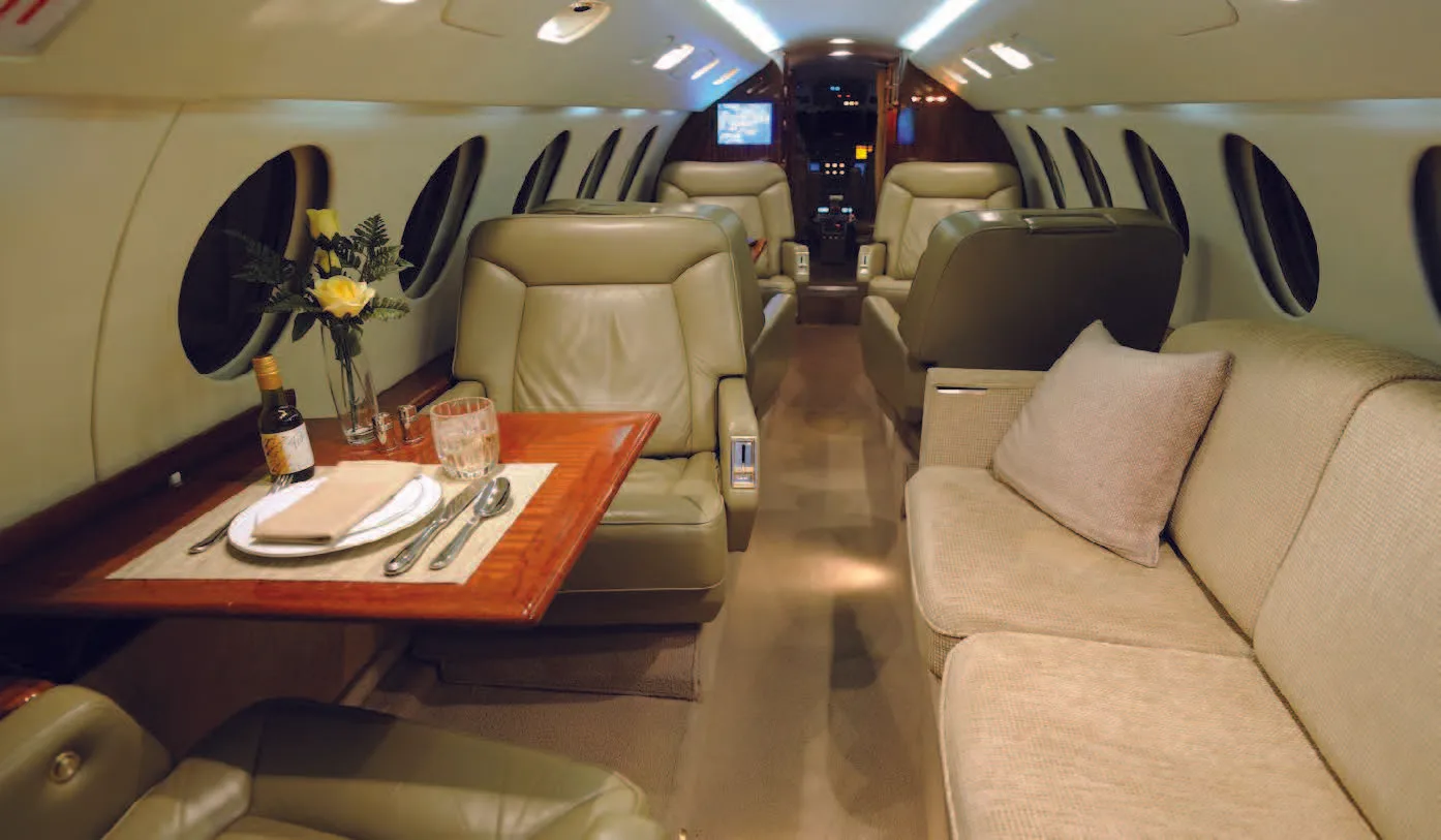 View of the aircraft's cabin interior with leather seats, a table setting, and a sofa.
