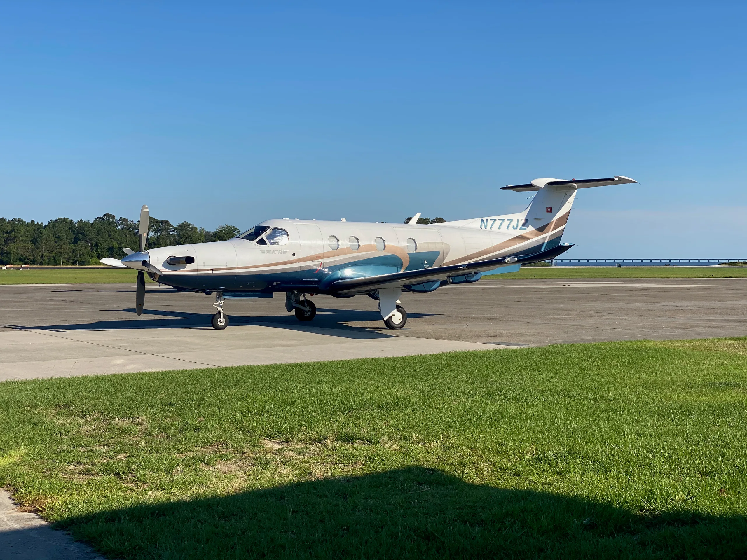 A Pilatus PC-12 aircraft with registration N777JZ is parked on the tarmac with a blue and brown paint scheme.