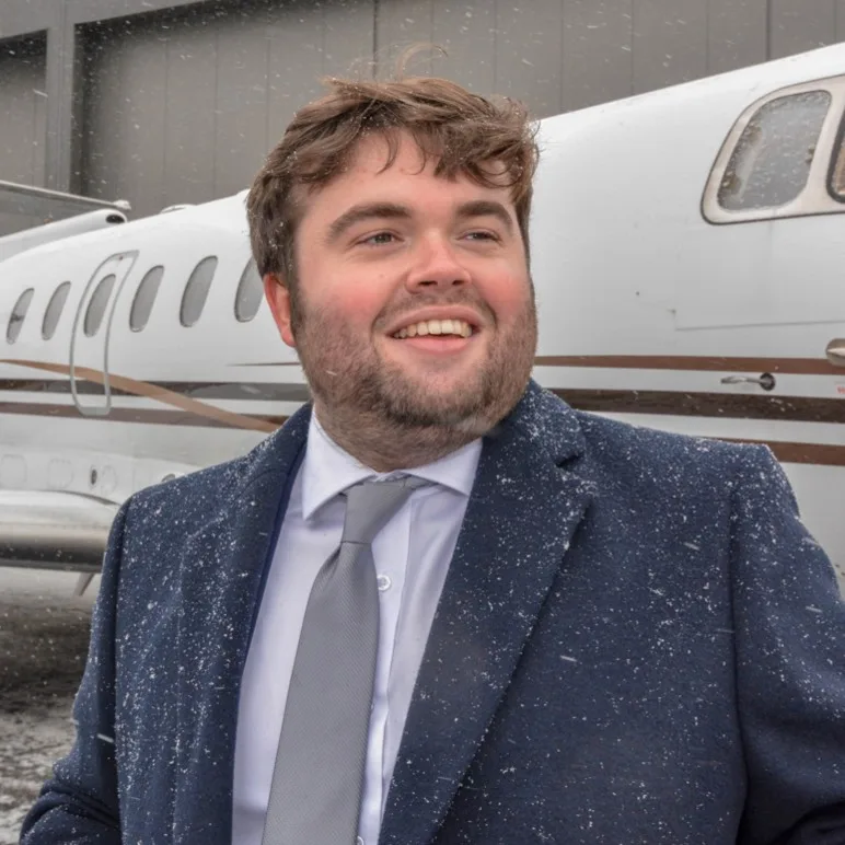 A man in a suit stands in front of a white jet aircraft in the snow.