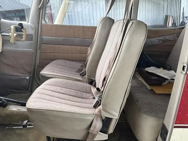 The interior cabin of a small aircraft, showing two rows of beige and brown fabric seats with seatbelts.