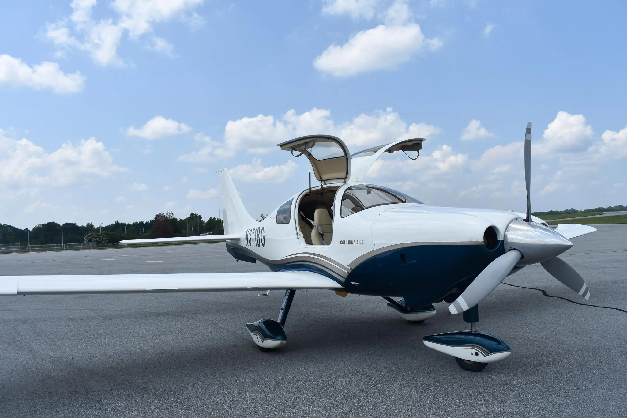 A white and blue Columbia 400 aircraft, registration N371BG, with its gull-wing doors open, parked on an airfield.