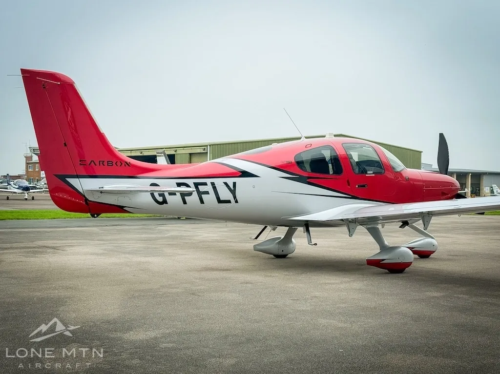 A red and white Cirrus SR22 aircraft (G-PFLY) viewed from the rear-side on a tarmac.