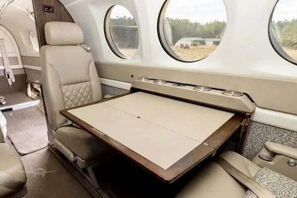 A close-up view of the aircraft's interior cabin showing a fold-out table and beige leather seating.